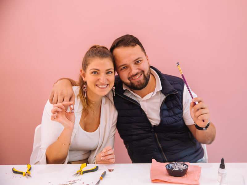 Smiling couple holding paint brush and earrings up to camera